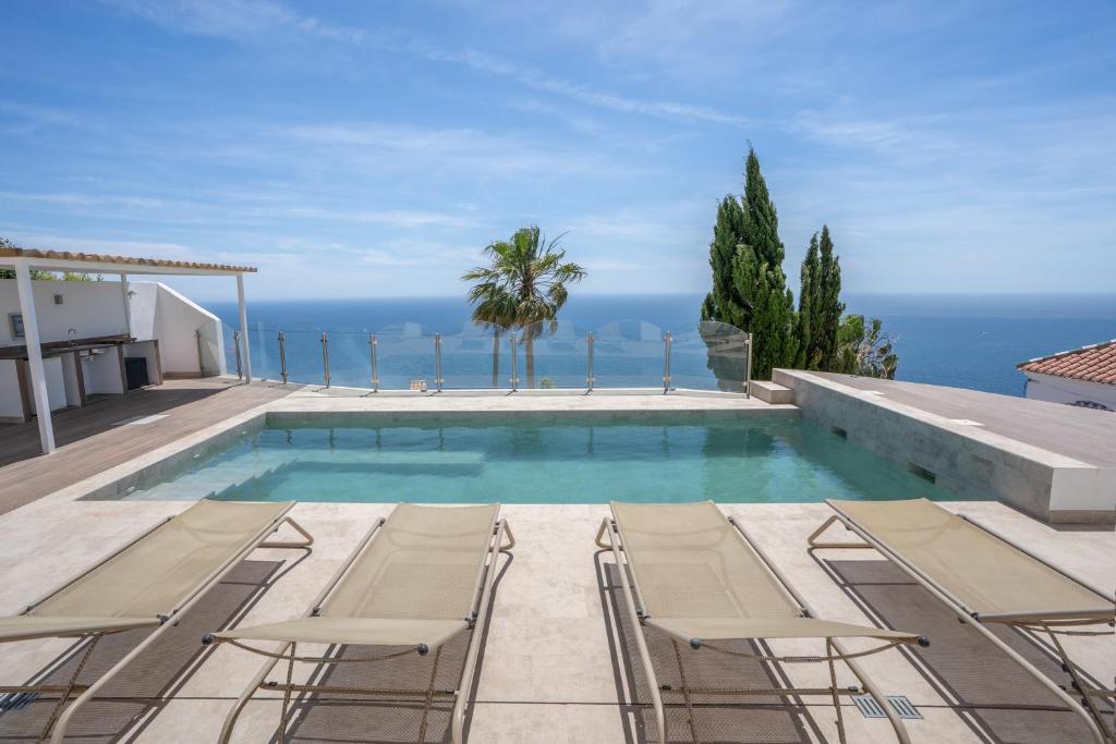 a swimming pool with chairs and the ocean in the background at Villa Quietud in Salobreña
