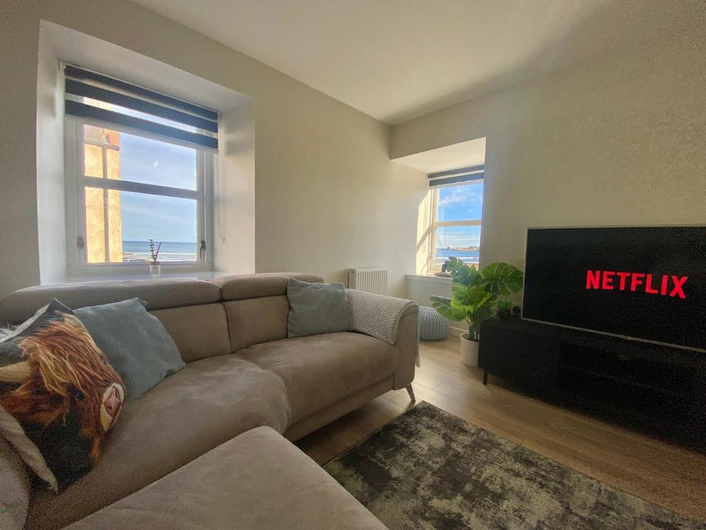 a living room with a couch and a television at Beach View, 3 The Granary in Banff