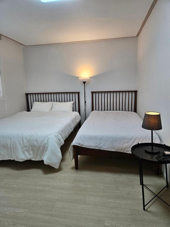 two beds in a bedroom with a lamp and a table at Hongdae ssuny house in Seoul