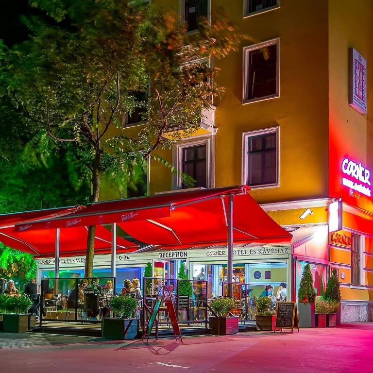 a restaurant with a red umbrella in front of a building at Corner Hotel & Kávéház in Dunaújváros