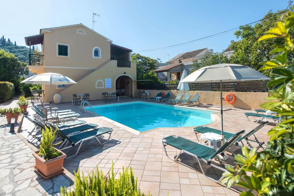 a pool with chairs and umbrellas next to a house at Ariti Apartments in Kassiopi