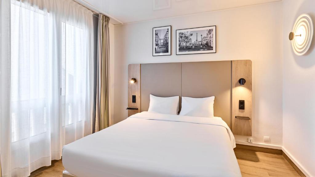 a bedroom with a large white bed and a window at Campanile Prime - Paris 14 Maine Montparnasse in Paris