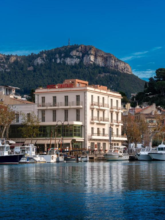 a building with boats in the water with a mountain at Hôtel Liautaud Cassis by Germain Collection in Cassis