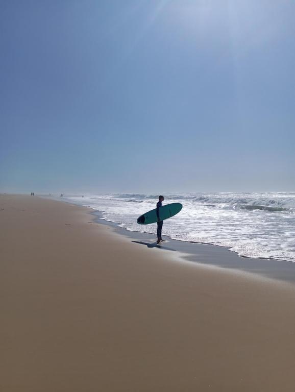 a man standing on the beach holding a surfboard at maison wave in Léon