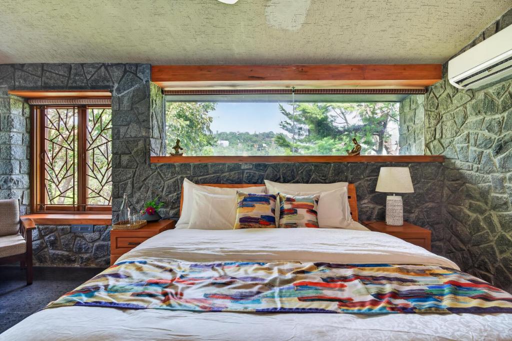 a bedroom with a large bed with a stone wall at SaffronStays Blooming Stone in Kotagiri