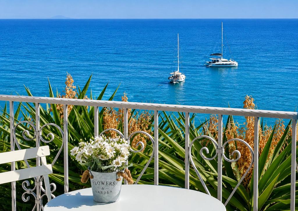 a table with a vase of flowers on a balcony with boats at Kalimera Aegina in Agia Marina Aegina
