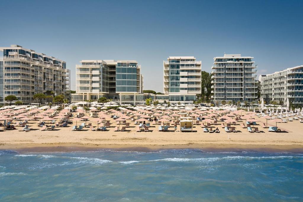a beach with chairs and umbrellas and buildings at Falkensteiner Hotel & Spa Jesolo in Lido di Jesolo