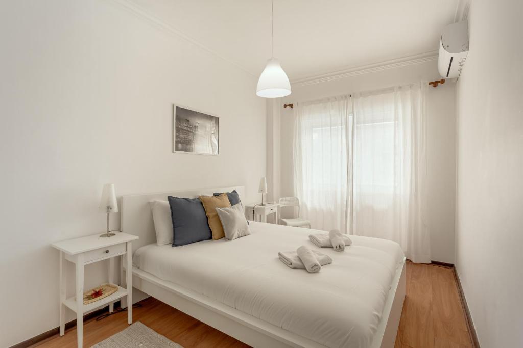 a white bedroom with a white bed with blue pillows at Almada Central by Homing in Almada