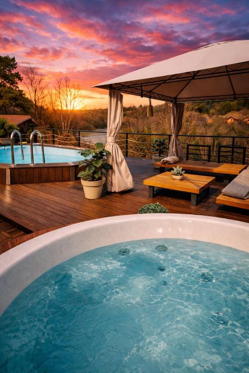 a hot tub in the middle of a deck with a sunset at La Casa Kiara - Heated Pool, Jacuzzi & Forest View in Stubicke Toplice