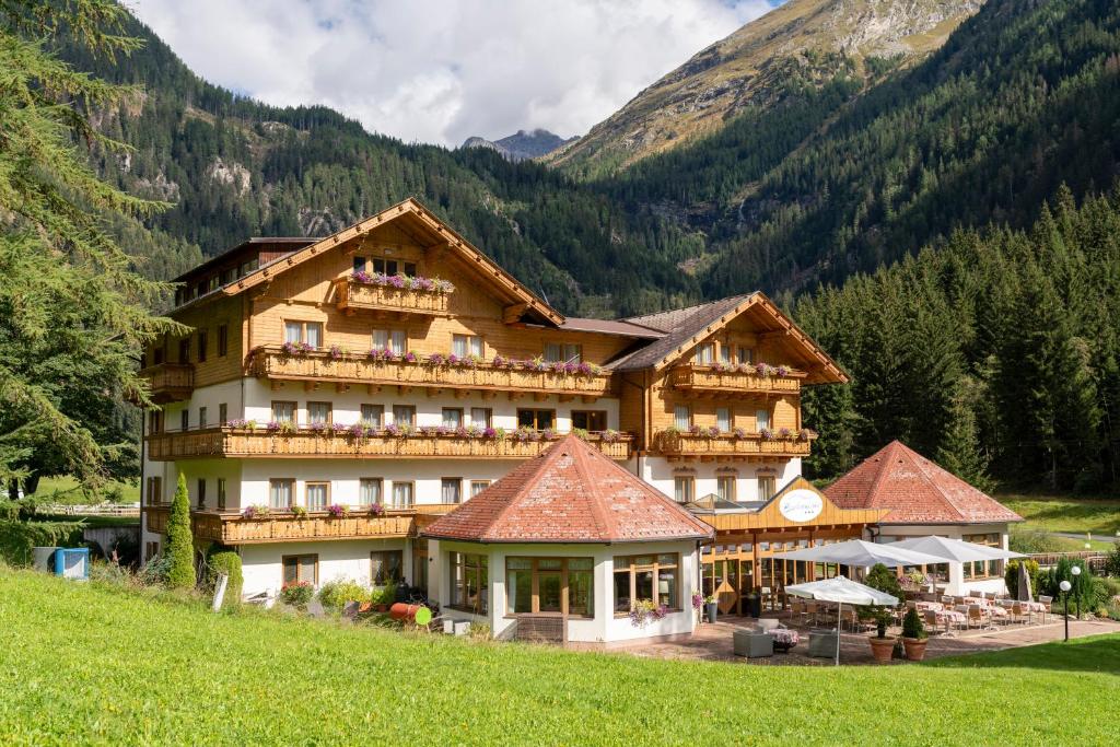 a large building on a hill with mountains in the background at Alpenhotel Badmeister in Flattach