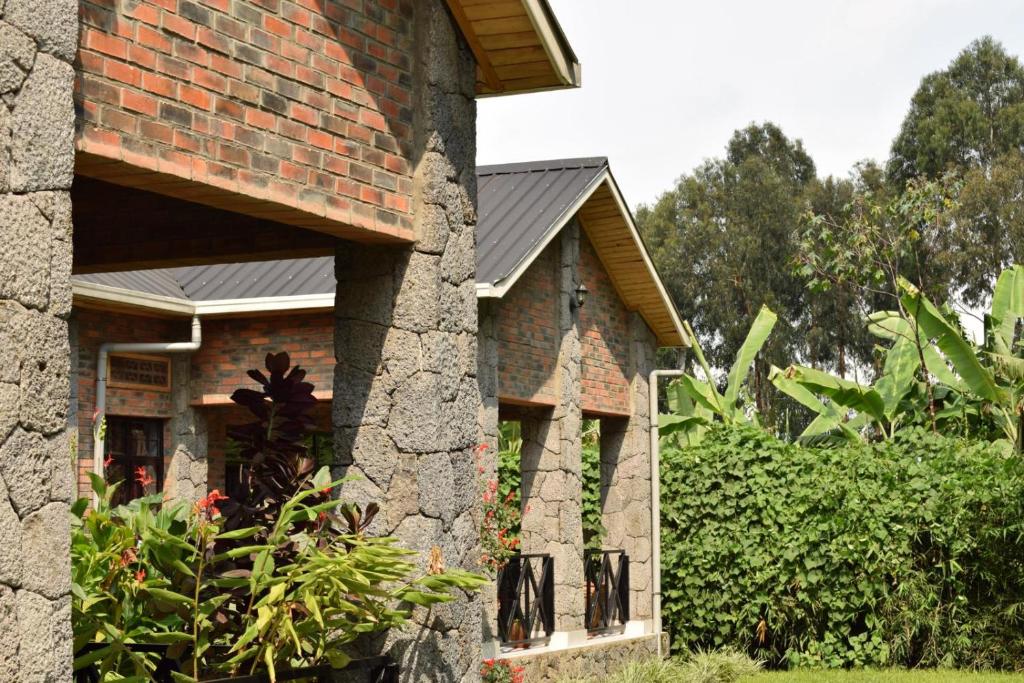 a brick house with a stone wall and bushes at Mrëmbo Boutik Hôtel in Ruhengeri