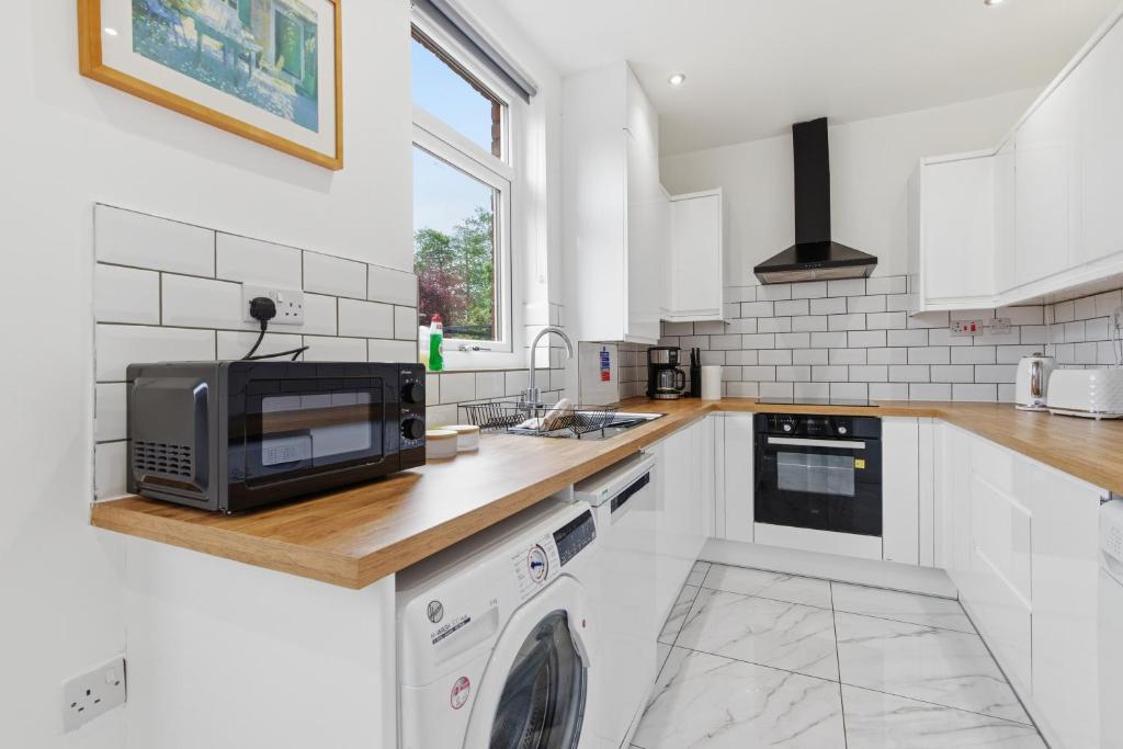 a white kitchen with a microwave and a sink at Large, Bright 4 Bed Home with Garden in Kenton