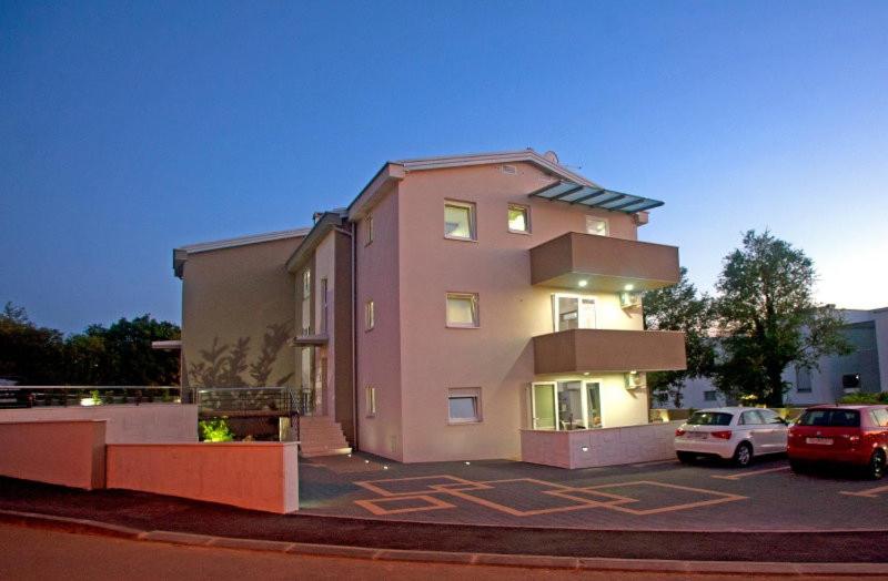 a pink building with cars parked in a parking lot at Apartmani Daška II in Njivice
