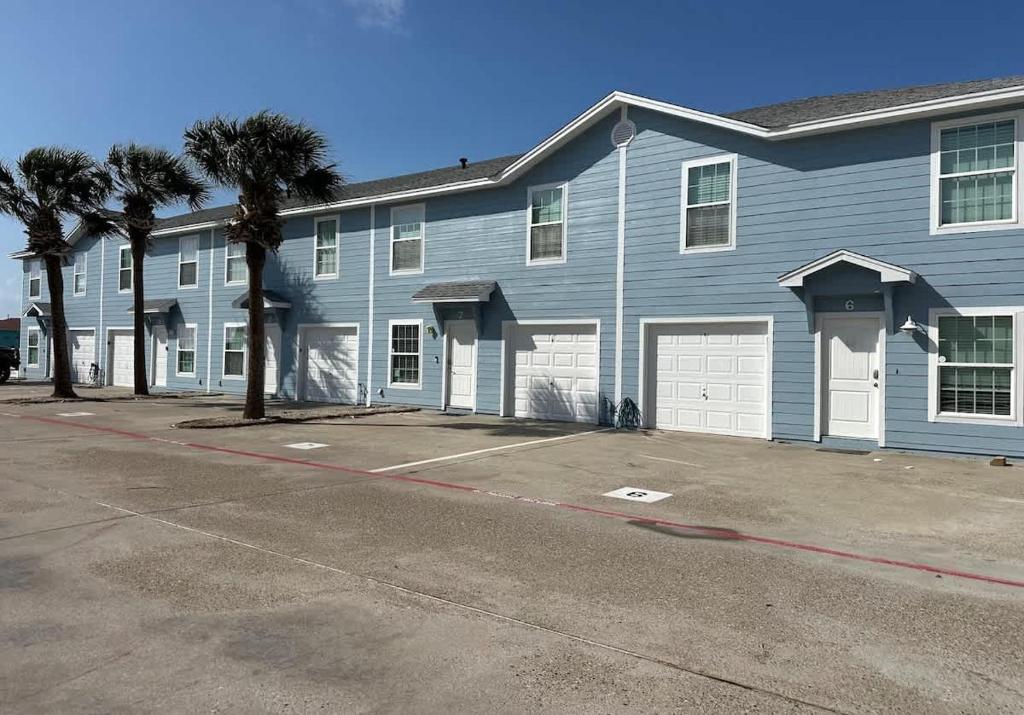 a blue building with two garage doors and palm trees at The Beach Peach in Port Aransas