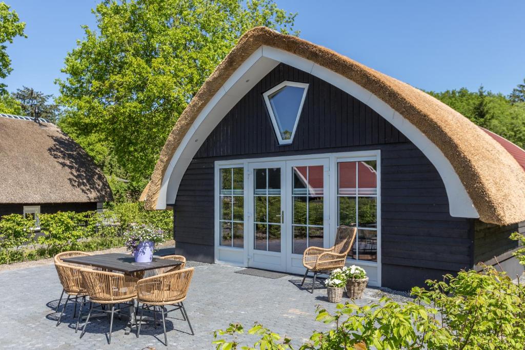a thatched roof house with a table and chairs at Residence de Eese in De Bult