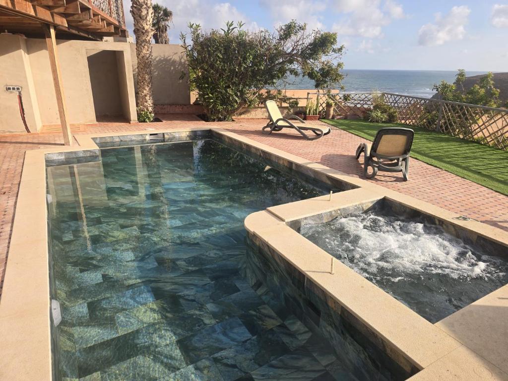 a swimming pool with two chairs in front of a house at Ocean View 6 bed Villa and Pool in Mirleft