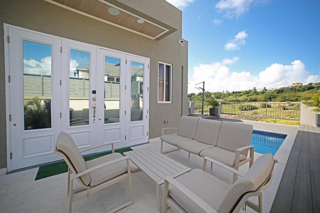 a patio with white chairs and a table and a pool at 3BR Modern Villa w/ Private Pool & Fire Pit in Saint Philip