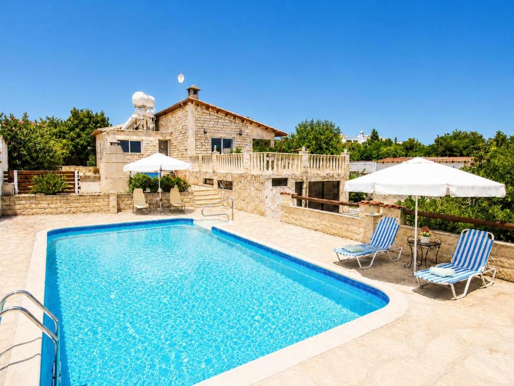 a pool with chairs and umbrellas in front of a house at Villa Stone House in Neo Chorio