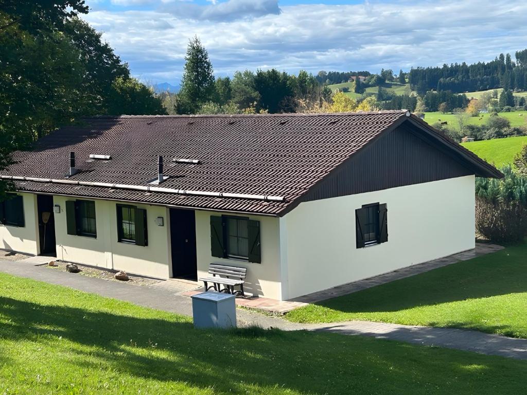 a white building with a black roof and a bench at Ferienhaus Lechseeidylle in Lechbruck