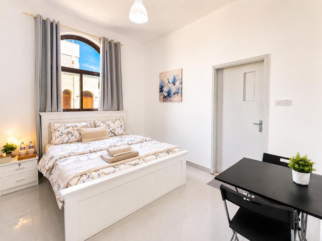 a white bedroom with a large bed and a desk at Flora Residence in Abu Dhabi