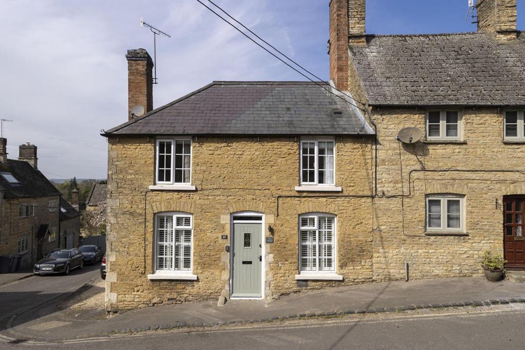 an old brick house with a white door on a street at The Smithy in Chipping Norton