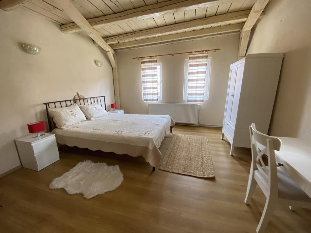 a bedroom with a bed and a desk and two windows at Fântânele Vacation Home, Charming Rustic Home in Fîntînele