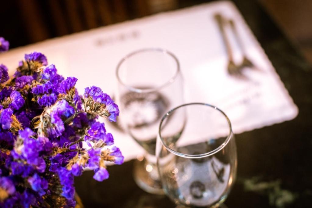 a table with two glasses and a bouquet of purple flowers at Zum Adler Castle B&amp;B in Jiaoxi