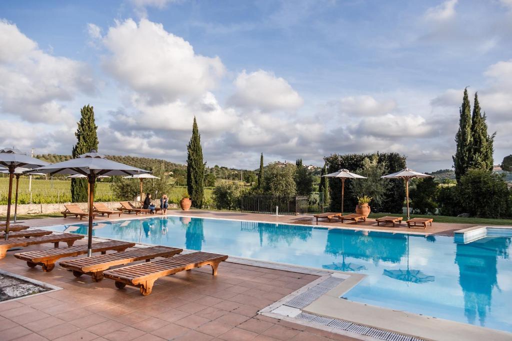 a large swimming pool with benches and umbrellas at Villa Acquaviva Wine Resort in Montemerano