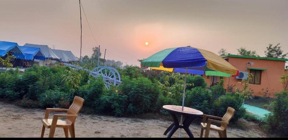a table and chairs with an umbrella in the rain at Bhitarkania Riverside Eco Resorts in Righāgarh