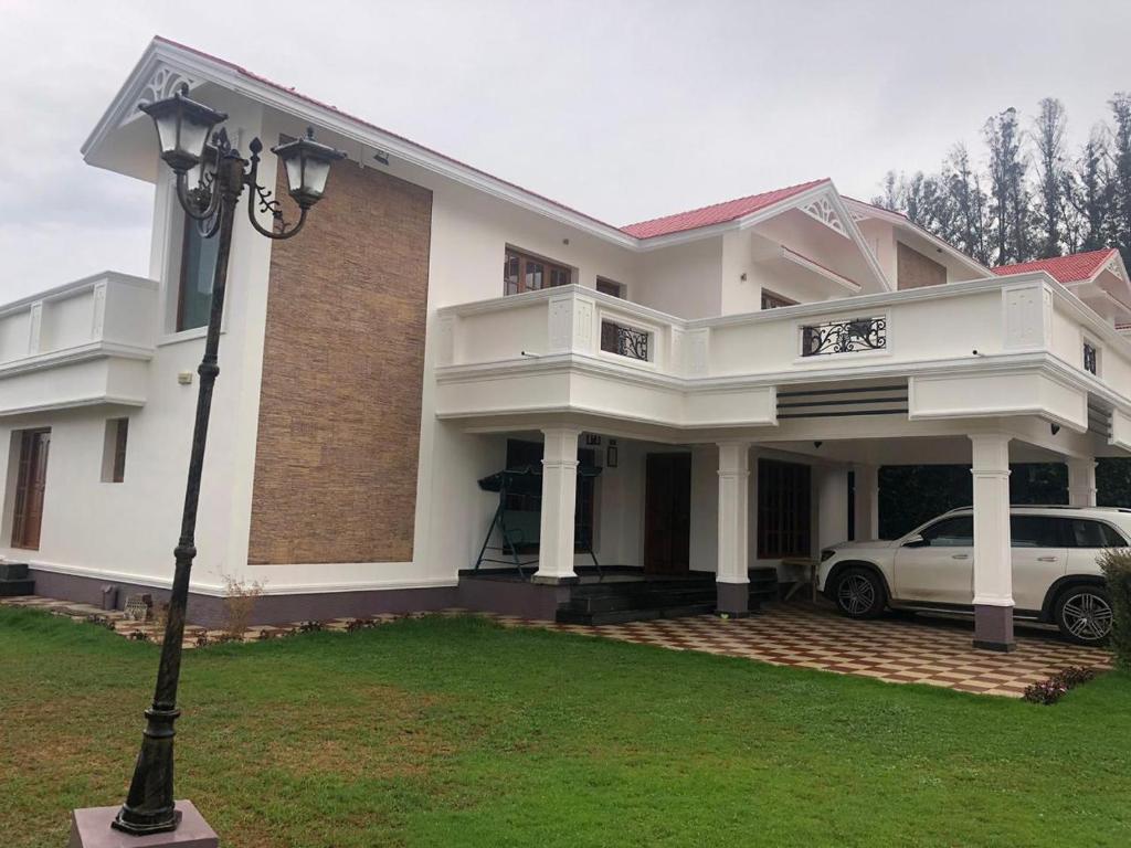 a white house with a car parked in the yard at Villa Bella in Ooty