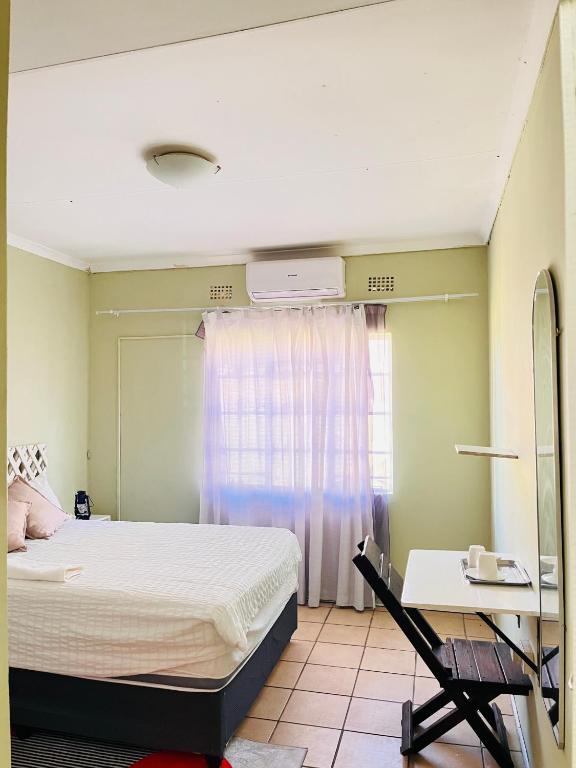 a bedroom with a bed and a desk and a window at Clock Inn Self Catering Accommodation in Gaborone