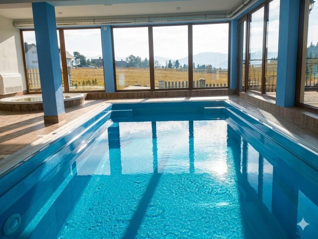 a swimming pool with blue water and windows at Hotel Góralski Raj in Nowy Targ