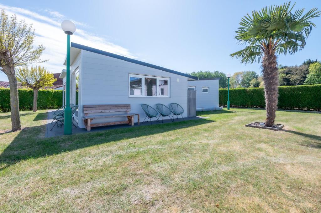 a small white house with chairs and a palm tree at Wonderful chalet in De Haan in De Haan