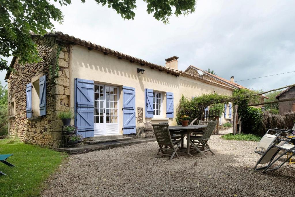 a table and chairs outside of a house with blue shutters at Gite La Forge in Le Buisson de Cadouin