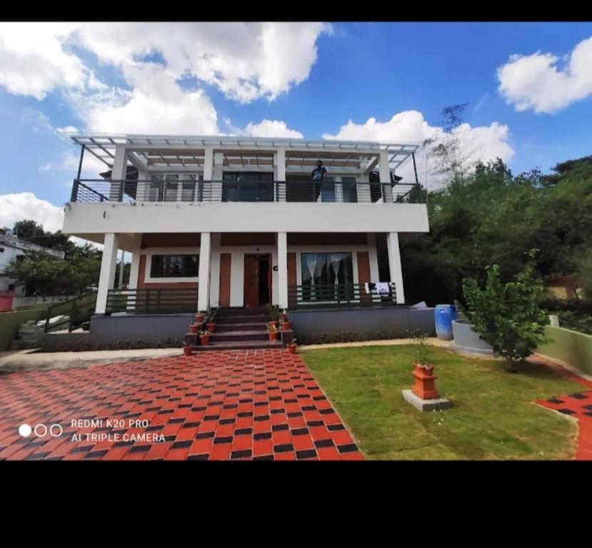 a large white house with a red brick yard at Assraya stay in Kushālnagar