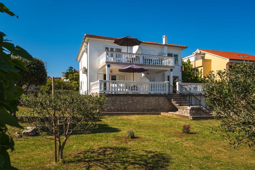 a white house with a balcony with an umbrella at Apartments Anka in Krk