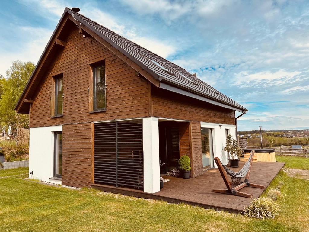 a house with a wooden deck with a chair on it at Na Kaszubskim Wzgórzu z sauną i banią in Garcz
