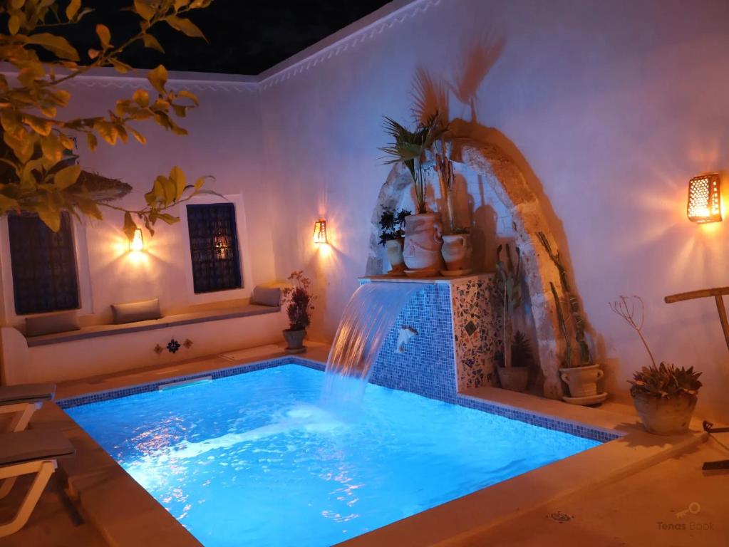 a swimming pool with a waterfall in a room at TenasBook Houch Yassmine in Erriadh