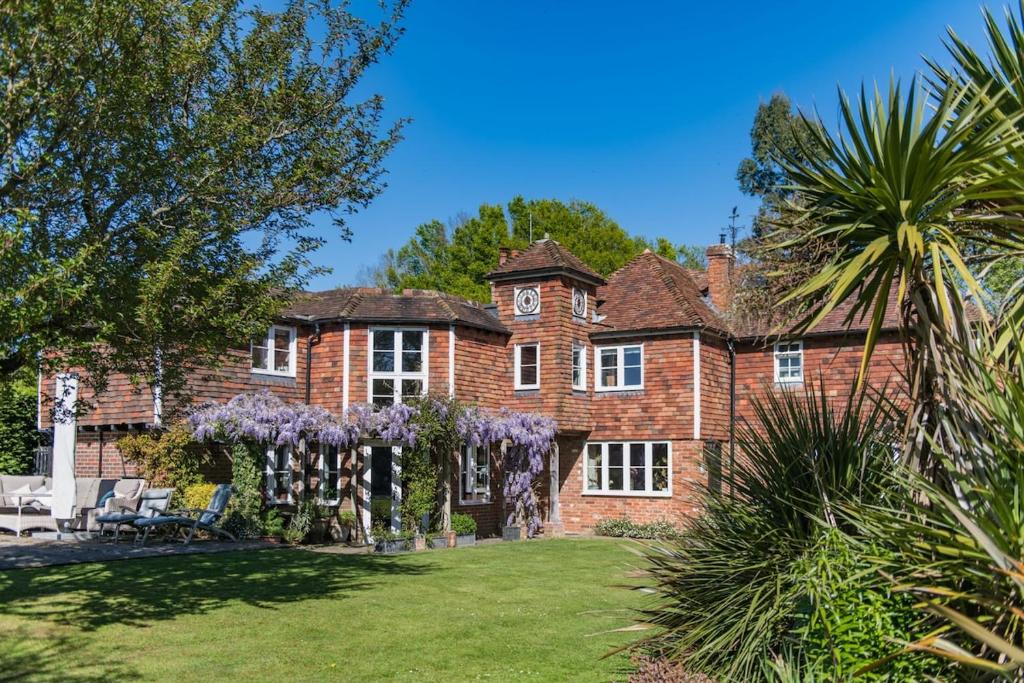 an old brick house with purple flowers in the yard at Lanes End by Keepers Cottages in Woodchurch