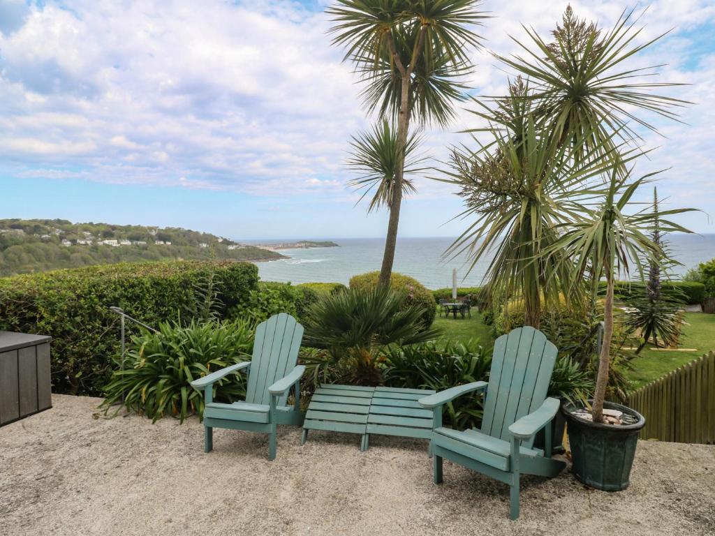 two blue chairs and a bench in front of palm trees at Apartment 1 Llewellan in Carbis Bay