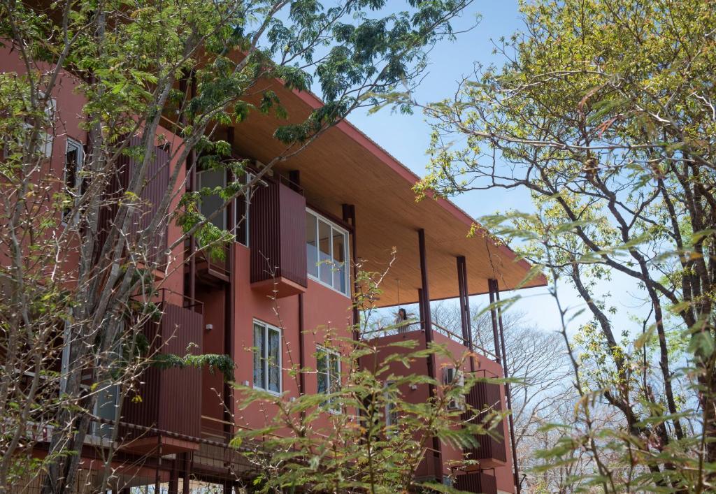 a red building with trees in the foreground at Tropical Design Stay near Playa Avellanas with Rooftop Terraces in Santa Cruz