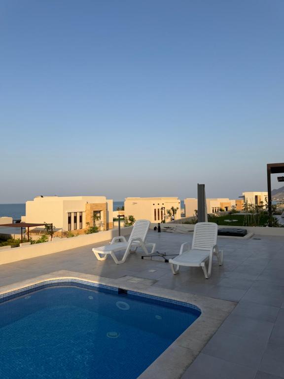 a swimming pool with two chairs and a table at Beach front 414 villa private pool in Muscat