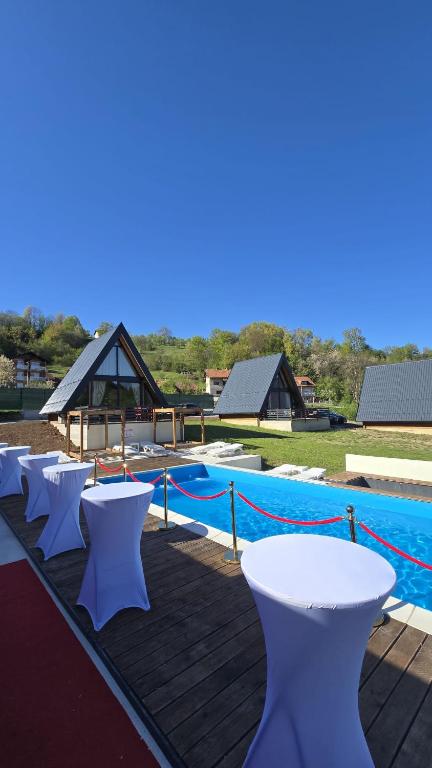 a row of white tables and chairs next to a pool at JAGI Bungalovi Mrkonjic Grad in Mrkonjić Grad