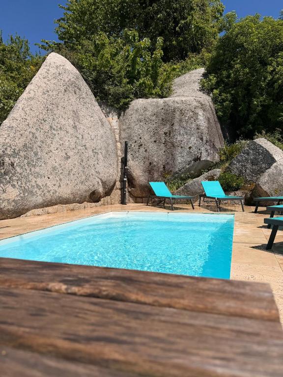 a swimming pool with two chairs and two large rocks at Hotel Clair de Lune in Zonza