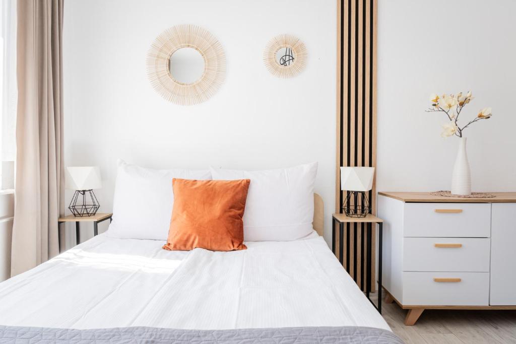 a bedroom with a white bed with an orange pillow at Willa Bliźniak - Pokoje i Apartamenty Bardzo Blisko Plaży in Karwia