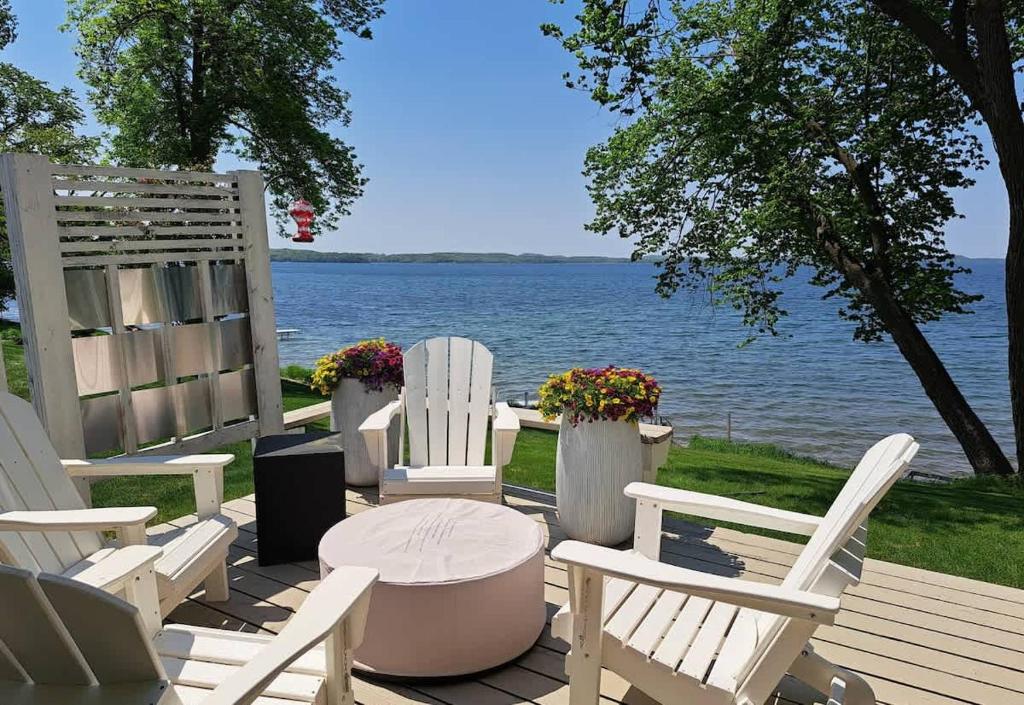 a deck with white chairs and a table and the water at NEW Sunset Cottage - Lake Lida in Pelican Rapids