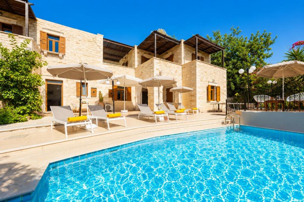a pool with chairs and umbrellas in front of a house at Villa Marcos Chara in Astérion