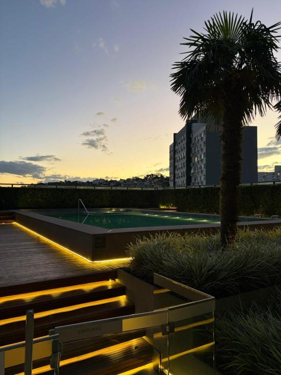a swimming pool with a palm tree and a building at Loft with pool and garage, next to Bourbon in Porto Alegre