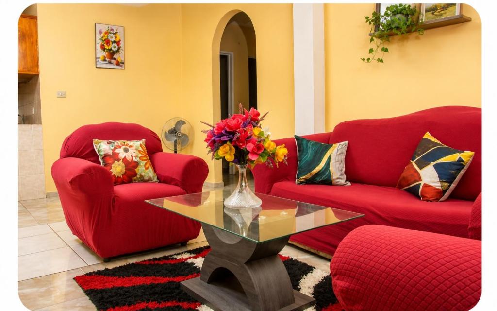a living room with two red chairs and a glass table at Scenic 3 Bedroom Apartment And Car Rentals in Canefield
