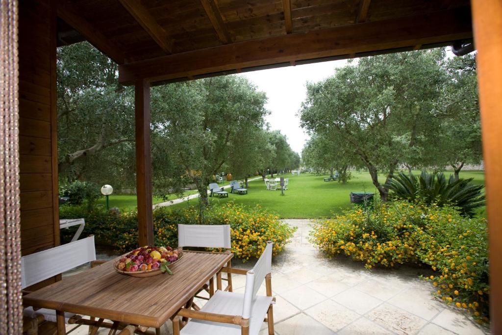 un portico con tavolo e sedie in legno e un parco di Azienda Agrituristica Scalelle a Otranto